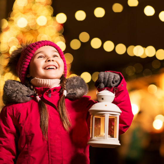 holidays, childhood and people concept - happy little girl with lantern at christmas market in winter evening