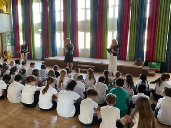 image shows children in school assembly with cllrs and officers presenting